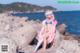 A woman in a bikini sitting on a rock by the ocean.