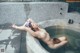 A naked woman laying in a bathtub with a bowl of water.