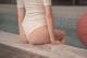 A woman in a white bodysuit sitting on the edge of a pool.