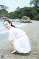 A woman in a white dress crouching on a beach.