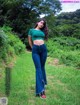 A woman in a green top and blue jeans standing in a field.